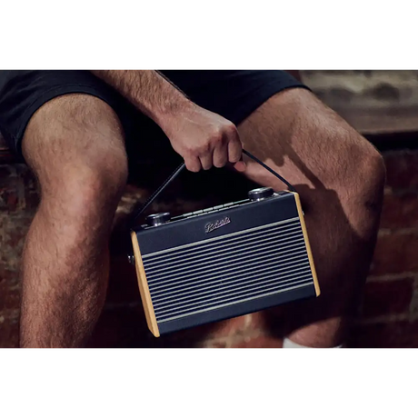 Man holding a Roberts Rambler Max Smart DAB+ FM radio with navy blue and tan wooden trim, featuring horizontal grille design and carrying handle