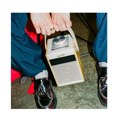 Roberts Rambler Midi DAB+ FM radio with Bluetooth in pastel cream being held by hands wearing blue jacket and black shoes, showing the device's speaker grille and dial interface