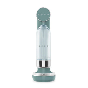 Smeg SKC01EGM sparkling water soda maker in emerald green with stainless steel accents, featuring a cylindrical design with clear water bottle chamber and rounded base