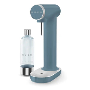 Smeg storm blue sparkling water soda maker with chrome-accented control dial, vertical carbonation chamber, white base, and matching clear glass bottle with stainless steel cap