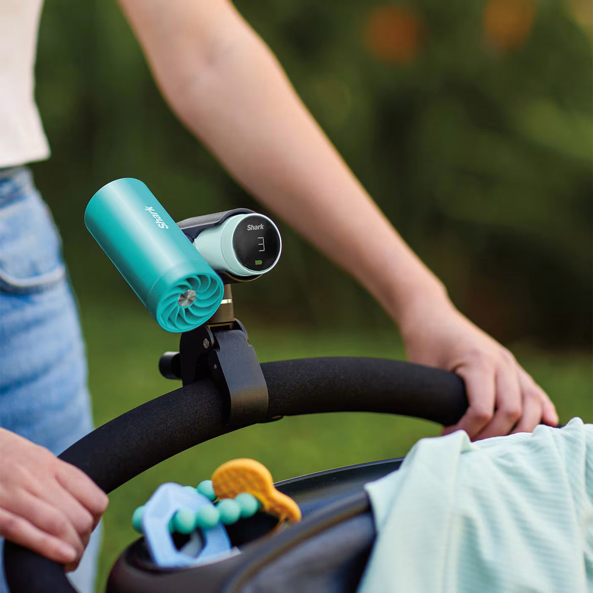 Baby stroller with a turquoise and black device attached, outdoors.