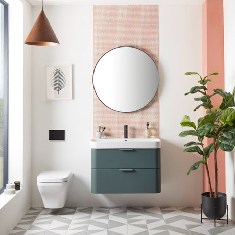 Modern bathroom vanity unit in Derwent Blue with white ceramic sink, circular mirror with dark frame mounted on pink brick backsplash, white toilet, geometric floor tiles, copper pendant light, botanical artwork, and potted plant