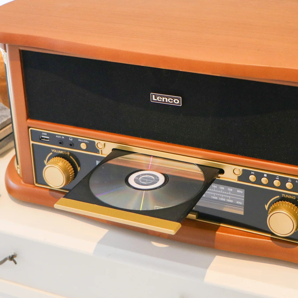 Lenco Classic Phono retro turntable record player in orange wood finish with CD player open showing disc, gold-tone controls including volume and tuning knobs, black speaker grille, and vintage-style design with USB and auxiliary inputs visible