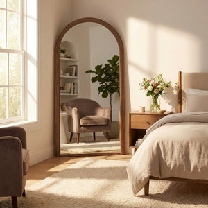 Tara Lane natural wood arched leaner mirror 80cm x 180cm in modern bedroom with cream bedding, wooden nightstand with flowers, and beige upholstered armchair reflected in mirror