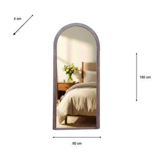 Tara Lane Stepped Arched Leaner Mirror 80cm x 180cm in natural wood frame leaning against bedroom wall, reflecting bed with white bedding and wooden nightstand with green flowers