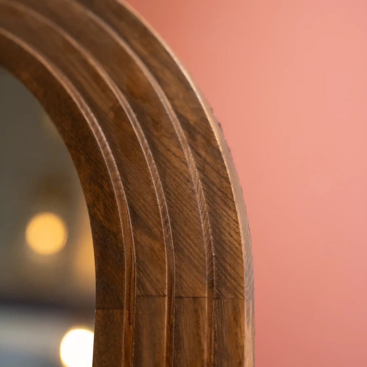 Close-up detail of natural wood grain on curved arched frame of Tara Lane stepped floorstanding mirror showing warm brown wood texture against pink background with soft lighting