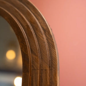 Close-up detail of natural wood grain on curved arched frame of Tara Lane stepped floorstanding mirror showing warm brown wood texture against pink background with soft lighting