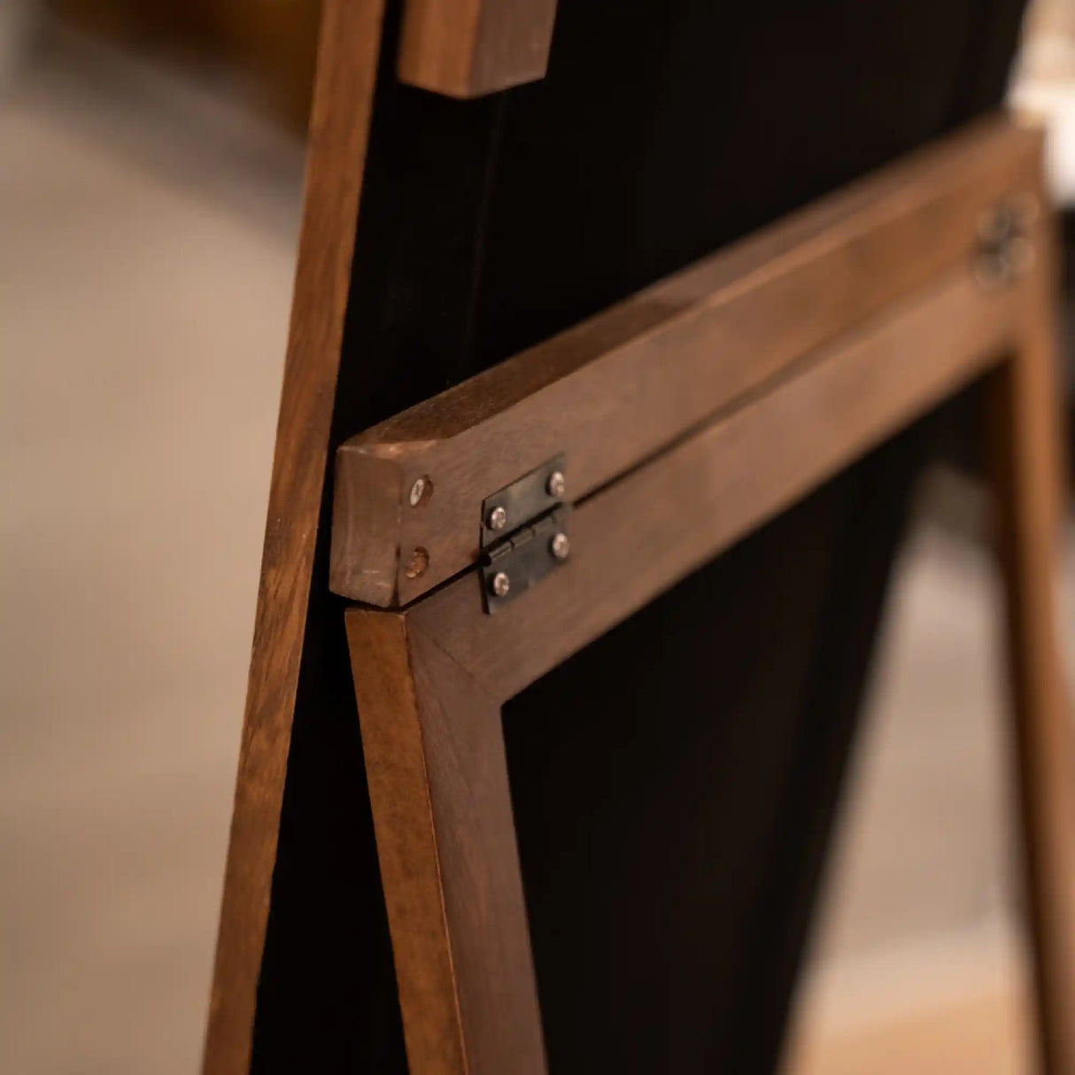 Close-up detail of wooden frame and brass hinge on a tall arched standing mirror showing natural wood grain and metal hardware