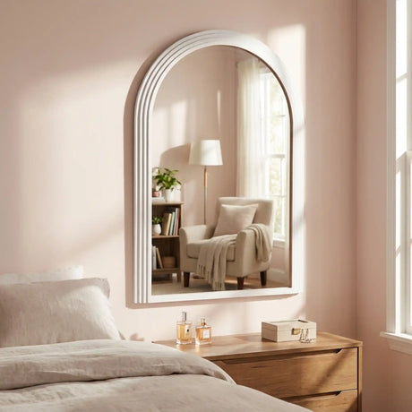 Tara Lane Stepped Arched Wall Mirror in oyster white mounted above wooden bedside table in modern bedroom with pink walls and natural lighting
