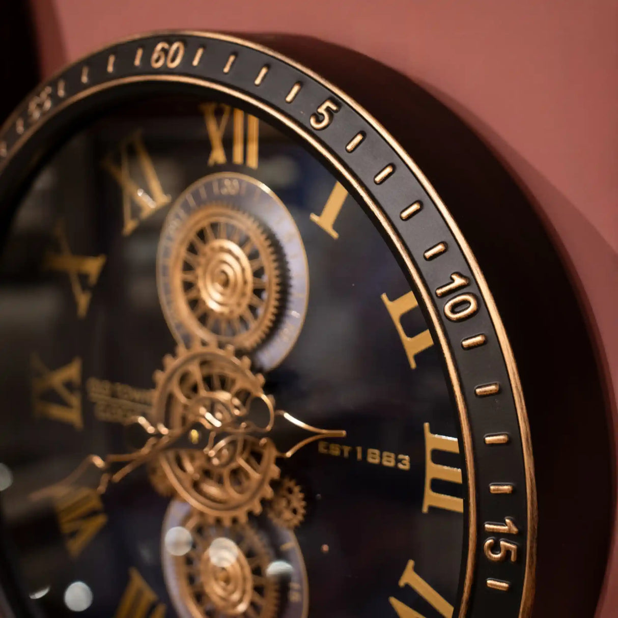 Tara Lane Old Town Gears Clock 50cm featuring black dial with gold Roman numerals, exposed brass gears and mechanical details against pink background
