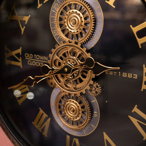 Tara Lane Old Town Gears Clock 50cm featuring ornate brass gears and mechanical clock hands on a black face with gold Roman numerals, established 1853