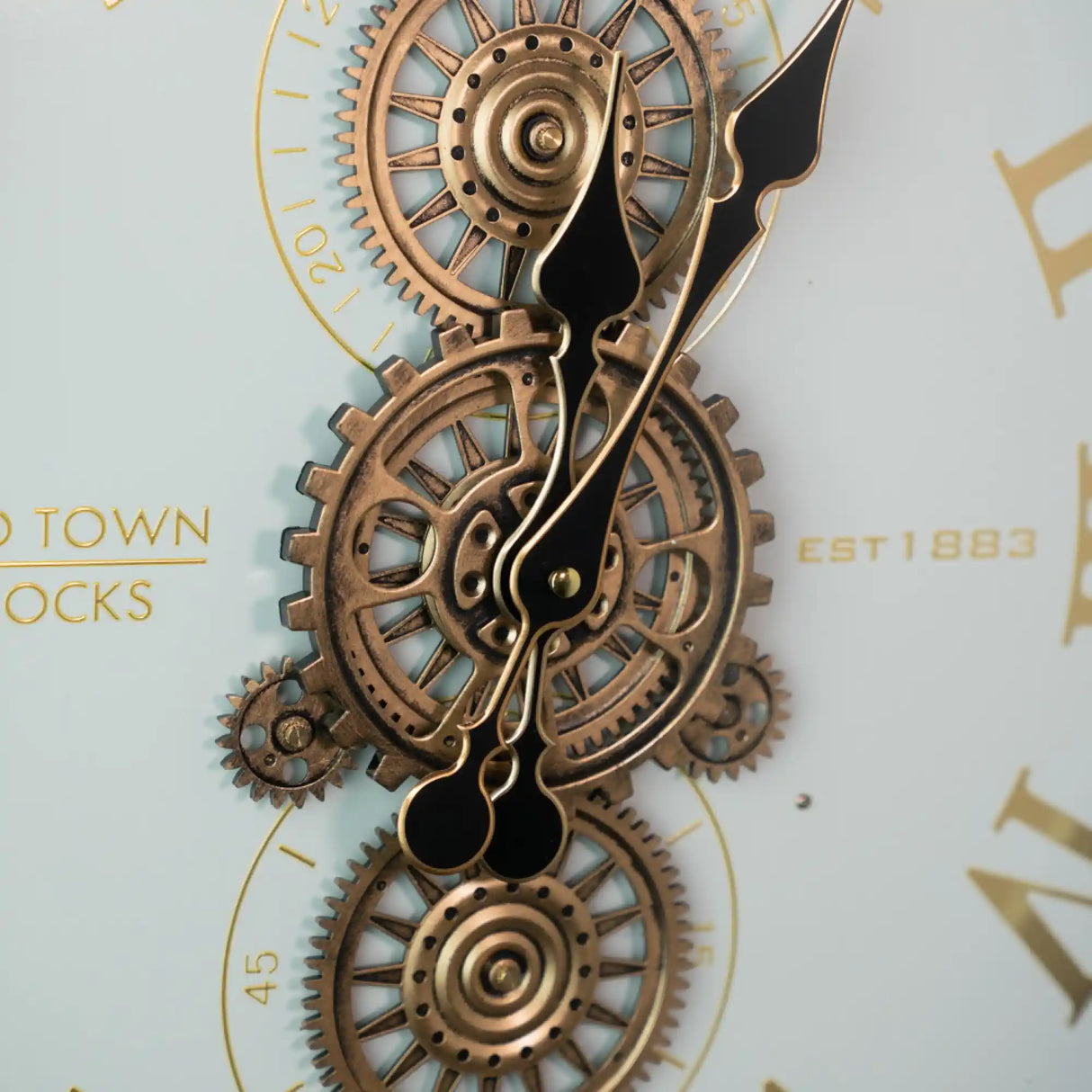 Steampunk-style wall clock with copper-colored brass gears and black ornate hands on ivory background, featuring industrial design with interlocking cogs and golden hour markers, 50cm diameter Tara Lane Old Town Clocks model