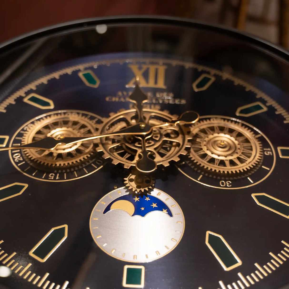 Close-up of Tara Lane Old Town Gears Clock Side Table showing ornate black dial face with gold Roman numerals, exposed brass gears and mechanisms, and moon phase complication in blue and white at 6 o'clock position
