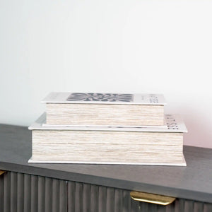 Two white decorative storage boxes with cream-colored pages stacked on a dark grey shelf, featuring modern minimalist design with geometric patterns on the top box
