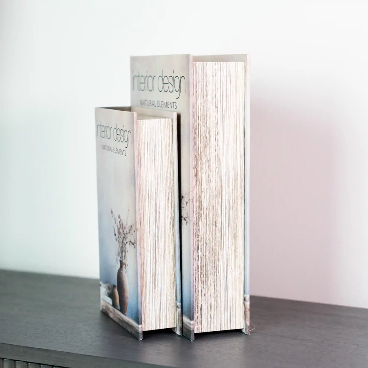 Two decorative book boxes in white with natural wood grain texture displayed on a dark surface against a white background, featuring Tara Design branding and botanical imagery on the spine, part of the Interior Design collection