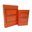 Two bright orange hardcover books from Tara Lane's Book Box Set titled "The Book of Luxury - The Art of Invisible Details" with black bordered frames on covers, standing together displaying spine and front cover details, labeled as Design Compendium