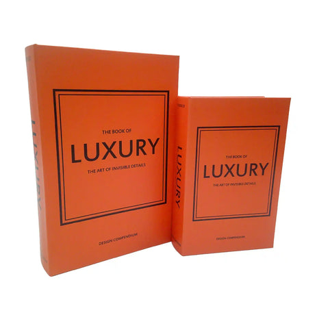 Two bright orange hardcover books from Tara Lane's Book Box Set titled "The Book of Luxury - The Art of Invisible Details" with black bordered frames on covers, standing together displaying spine and front cover details, labeled as Design Compendium