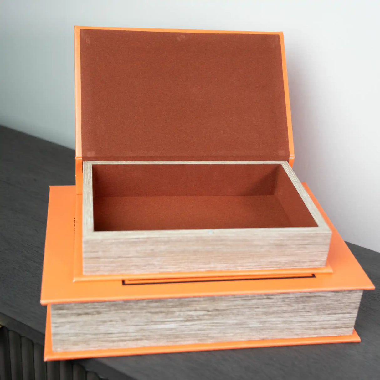 Two stacked decorative wooden book boxes with bright orange trim and natural wood sides, featuring terracotta-colored felt interiors, with the top box open to display storage space