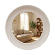 Large circular wall mirror with thick white oyster-colored frame reflecting a modern living room with beige sofa, wooden bookshelf, and natural window light