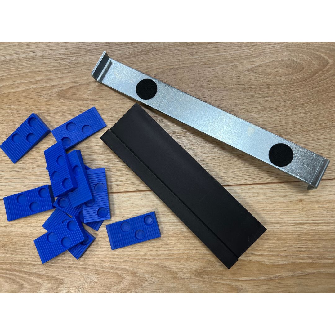 Trojan Wooden Floor Fitting Kit comprising a grey canvas strap with metal buckle and black circles, a black storage box, and multiple blue plastic spacer wedges on wooden flooring