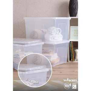 Wham 60 litre clear plastic storage box with lid displayed in a bedroom setting containing folded white bedding and textiles, featuring a geometric patterned wallpaper background and wooden flooring, with detail circle highlighting the included lid, BPA free and made in Britain