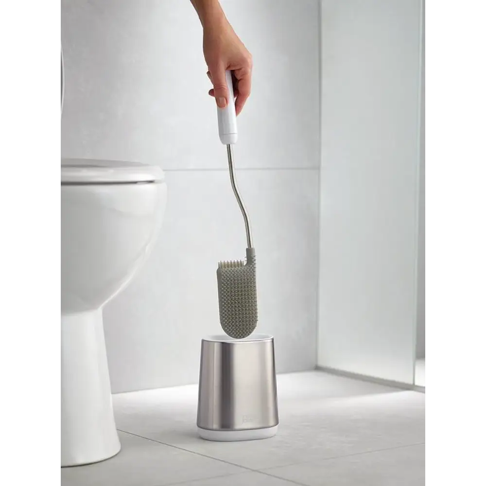 Joseph Joseph Flex Lite Steel Toilet Brush with white handle and stainless steel holder displayed in modern bathroom next to white toilet