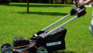 WORX 40V Brushless self-propelled lawn mower with 46cm cutting deck in black and orange, shown on green grass with operator holding handle bar and batteries visible