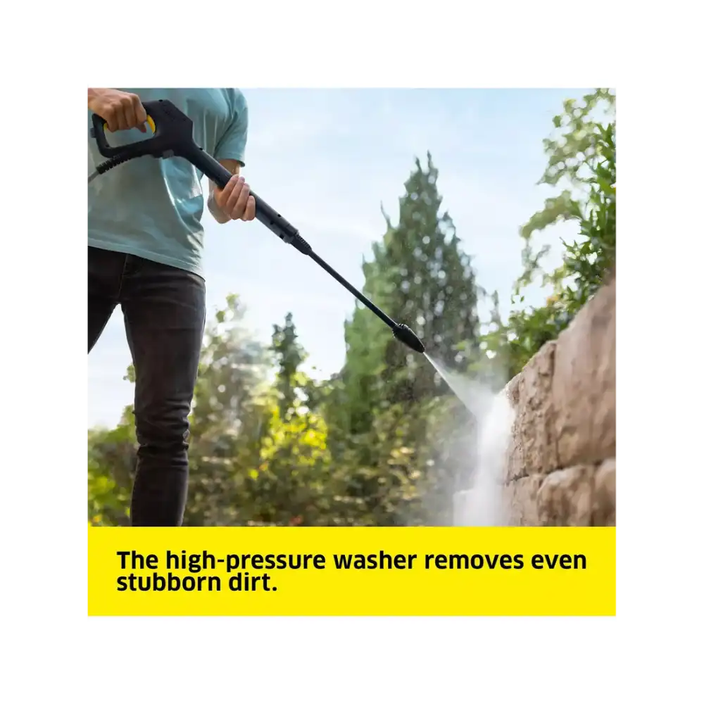 Person in light blue shirt using Karcher K5 high-pressure washer to clean brick wall with trees in background demonstrating powerful water jet removing stubborn dirt