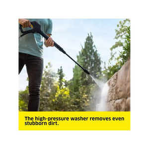 Person in light blue shirt using Karcher K5 high-pressure washer to clean brick wall with trees in background demonstrating powerful water jet removing stubborn dirt