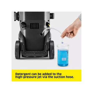 Karcher K5 pressure washer with detergent being added through suction hose from blue measuring beaker, demonstrating cleaning solution application method