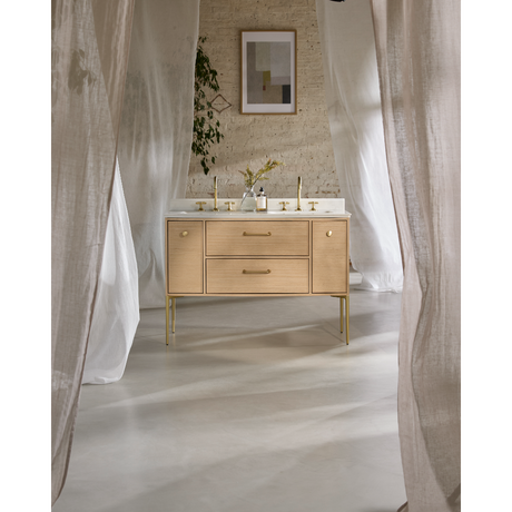 Light oak vanity unit with white marble countertop and brass fittings in modern bathroom with sheer white curtains and brick wall backdrop