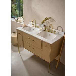 Double basin bathroom vanity unit in light oak wood with white marble countertop, brass faucets and handles, featuring two rectangular ceramic sinks with decorative accessories and potted plant