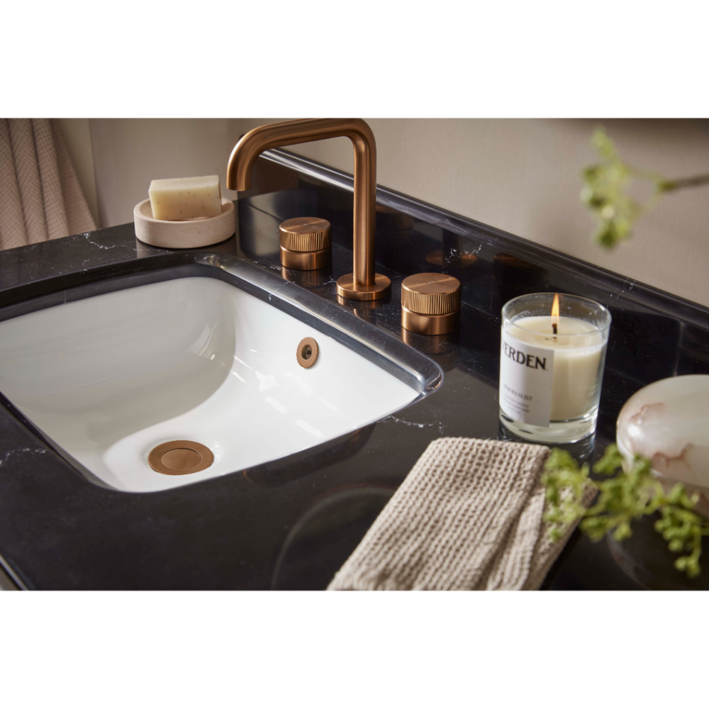 Modern bathroom vanity with white ceramic curved sink, black marble countertop, brushed bronze tap and faucet handles, soap dish, scented candle, gray towel and green plant decoration