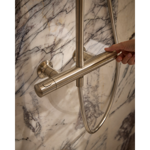 Close-up of a modern brushed nickel shower system with cylindrical bar rail mounted on marble tile wall, showing hand adjusting the rail fixture against veined white and grey marble background