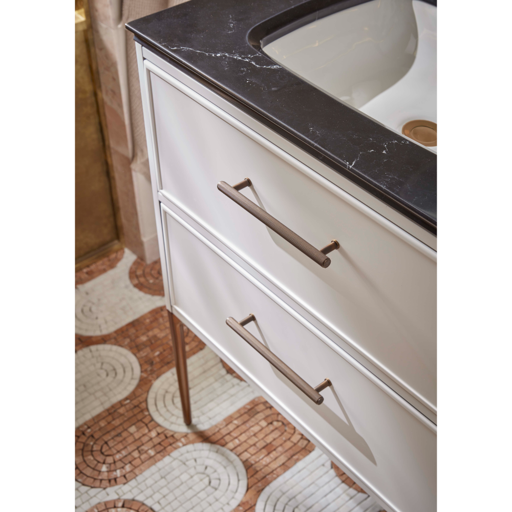White bathroom vanity unit with dark countertop, bronze handles, and drawers displayed in a bathroom setting with terracotta and cream mosaic tile flooring