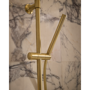 Roper Rhodes Walcot concealed shower system in brushed brass with cylindrical bar valve and sliding hand shower bracket against marble tiled bathroom wall