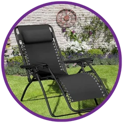 Black lounge chair on grass with a garden and brick wall in the background