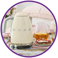 Cream-colored kettle with 'Smeg' branding on a table with a glass of juice and strawberries.