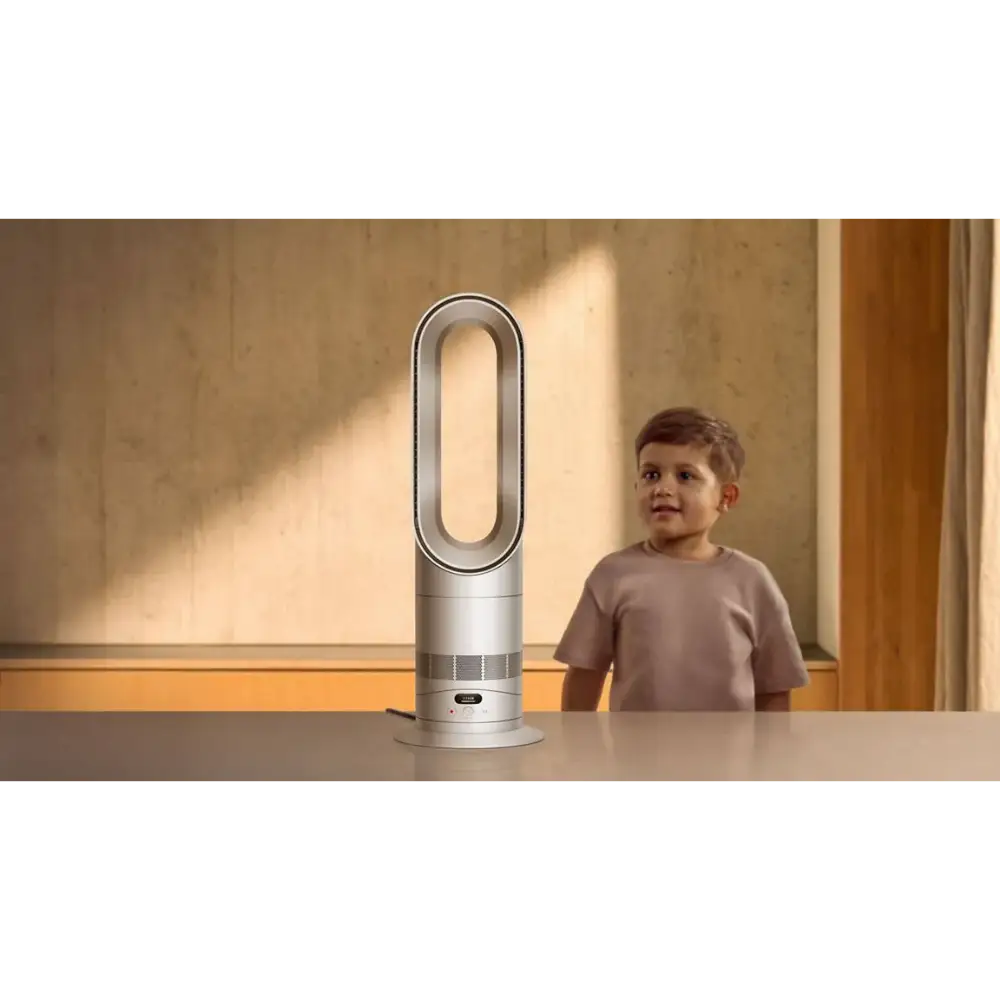 White and silver Dyson Hot + Cool HF1 heater and fan with oval-shaped opening displayed on a table next to a young child in a beige room with wooden door