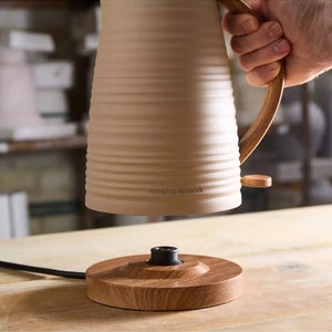Morphy Richards Clay Felspar electric jug kettle in cream and wood finish being held over its matching wooden base, displaying the modern design with brown wood-effect handle and accents on a kitchen countertop