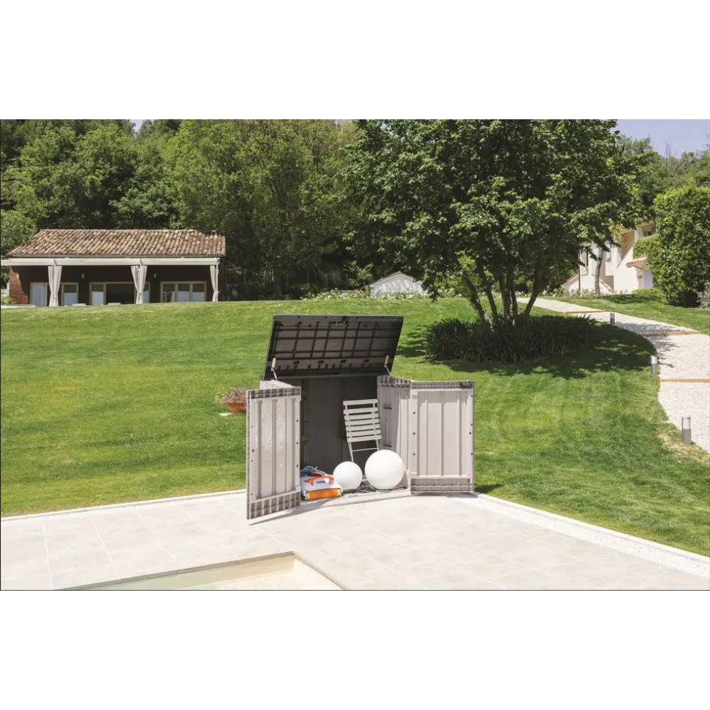 Toomax Storer Plus garden storage unit in taupe grey and anthracite with open lid displaying stored garden tools and equipment on a patio, surrounded by manicured lawn and trees