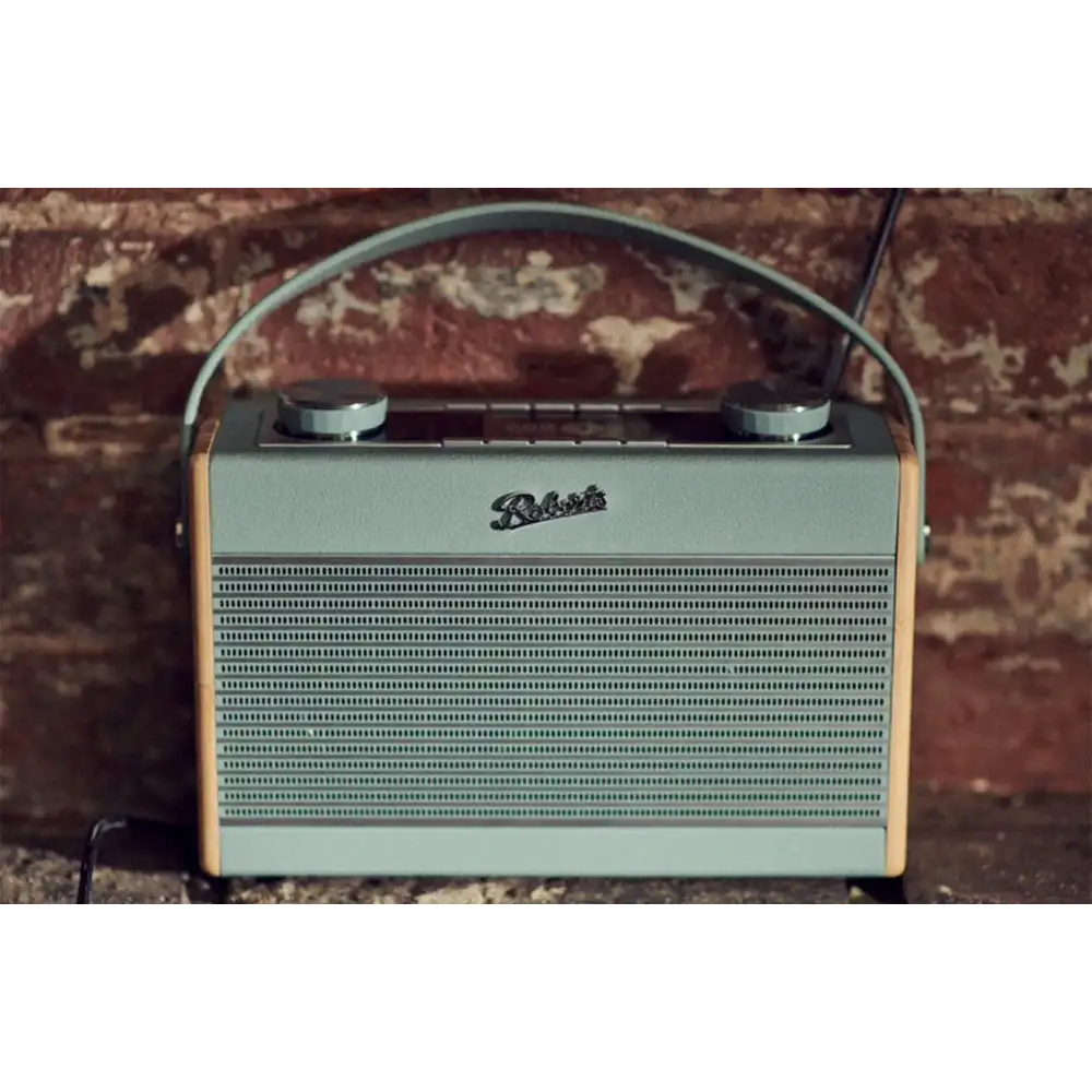 Roberts Rambler Max Smart DAB+ FM radio in duck egg blue with tan leather trim and carrying handle, displayed against a patterned brick background