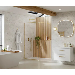 Modern bathroom featuring Merlyn 6 Series Sleek framed wetroom panels in brushed brass with vertical wood slat detailing, paired with white vanity unit, rounded mirror with brass frame, terrazzo-style walls, skylight, and contemporary fixtures in a minimalist Scandinavian design