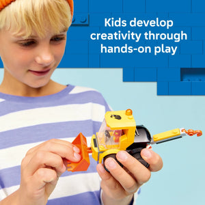 Young child with blonde hair wearing a purple and white striped shirt playing with a yellow and orange LEGO construction loader toy against a blue background, demonstrating hands-on creative play with the LEGO Rides Construction Loader set 60483