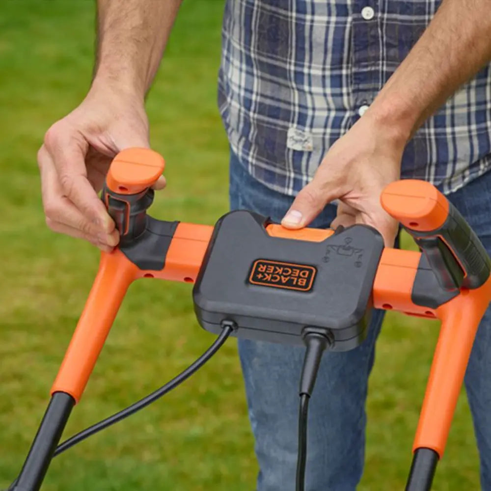 Man holding orange and black Black & Decker electric lawnmower with 32cm cutting width outdoors on grass, showing handle grips and power cable