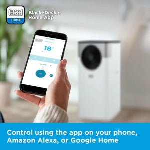 Hand holding smartphone displaying Black+Decker Home App with 18°C temperature setting and ON button, showing control interface for white portable air conditioner unit with dark compressor visible in blurred background