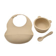 Beige silicone bib, bowl, and spoon set on a white background