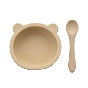 Beige silicone feeding set for babies featuring a round bear-shaped bowl with cute facial details and a matching soft-grip spoon, displayed on white background