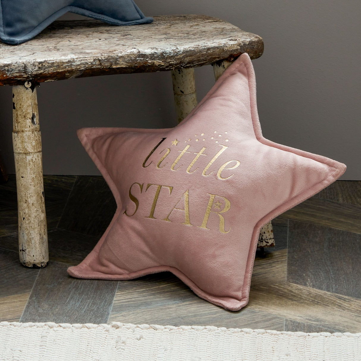 Bambino Little Star Velvet Cushion in blush pink with gold embroidered text, displayed on rustic wooden bench with weathered finish