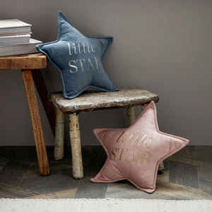Blue velvet star-shaped cushion with little star embroidered text displayed on rustic wooden stool next to pink matching cushion and stacked books